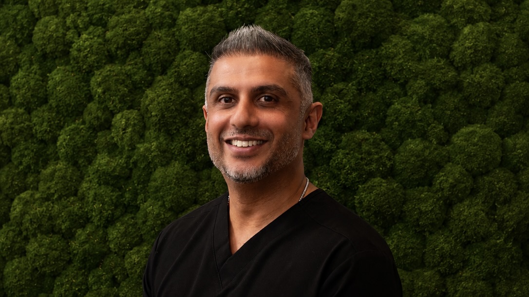 Man smiling wearing black in front of shrubbery